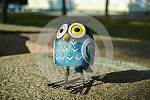 A close-up toy of a surprised blue owl with multi-colored eyes stands on a granite stone. The toy is illuminated by evening