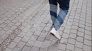 Close-up tracking shot of the legs of a man in white sneakers and a jeans walking confidently forward at the sidewalk on Tel Aviv