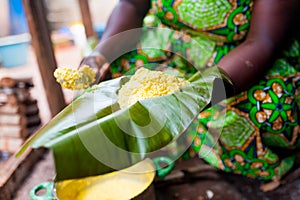 Close up of traditional african corn foufou on plantain leaf held by woman in traditional dress cooking