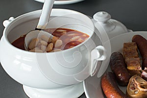 Close up of a traditional fabada home made. A ladling serving fabada from a bowl and side dish with the traditional compango, with photo