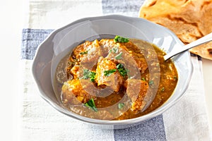 Close up traditional Indian butter chicken curry and lemon served with chapati bread on grey plate.