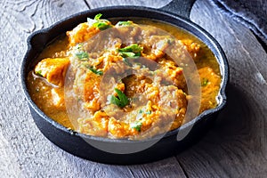 Close up traditional Indian butter chicken curry and lemon served with chapati bread in iron-cast. Wooden background.