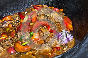 Close up of traditional Uzbek shurpa dish made from lamb and various vegetables at the open fire in cast iron cauldron