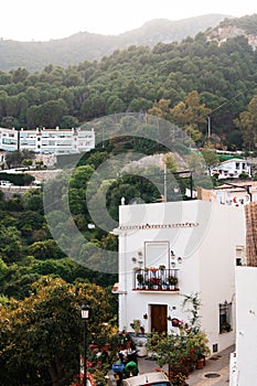A close-up of a traditional white home in Ojen with a flower-adorned balcony, set against the green Andalusian hillside
