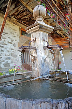 Close-up of a traditional wooden fountain located in Saint Veran village, with a traditional wooden house in the background