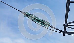 Close up of a transparent turquoise high voltage insulator or isolator in sunlight on electric tower on blue sky background.