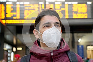 Close-up traveler man wearing KN95 FFP2 face mask at the airport. Young caucasian man with behind timetables board of departures