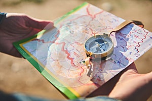 Close-up of traveler& x27;s hands holding map and using compass, searching direction while hiking, exploring nature