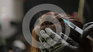 Close-up trichologist in gloves injecting syringe in female head. Unrecognizable Caucasian specialist treating hair skin