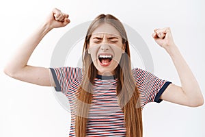 Close-up triumphing, joyfully young woman in striped t-shirt, raising hands up yelling, rooting for favorite team, close