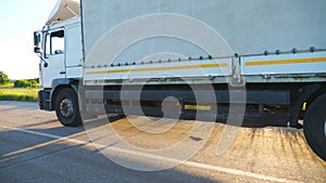 Close up of truck with cargo trailer driving on highway and transporting goods. White lorry speeding through countryside