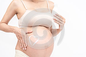 Close-up of tummy young pregnant model applying lotion on belly to prevent stretch marks. Future mom rubbing moisturizing cream on