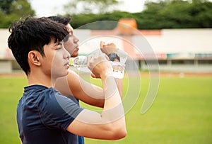 Close up two Asian teenages drinking water from bottle after run  in park