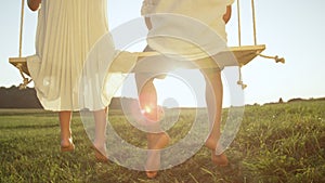 CLOSE UP Two barefoot young kids sitting on wooden swing at warm golden sundown