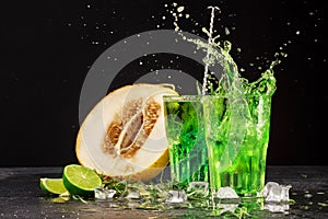 Close-up of two bright tarragon splashing cocktails on a black background. Drinks with tarragon, cut sweet melon, ice cubes, and