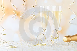 A close up of two champagne flutes filled with champagne for a celebration, against a golden bokeh background.