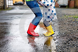Close-up of two children, toddler girl and kid boy wearing red and yellow rain boots, walking during sleet. Happy