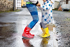 Close-up of two children, toddler girl and kid boy wearing red and yellow rain boots, walking during sleet. Happy