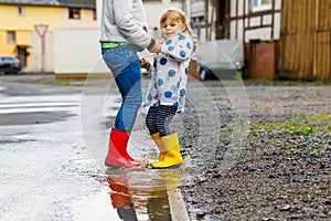 Close-up of two children, toddler girl and kid boy wearing red and yellow rain boots, walking during sleet. Happy