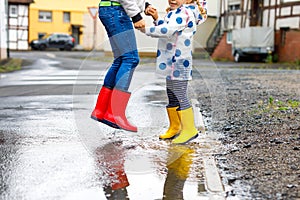 Close-up of two children, toddler girl and kid boy wearing red and yellow rain boots, walking during sleet. Happy