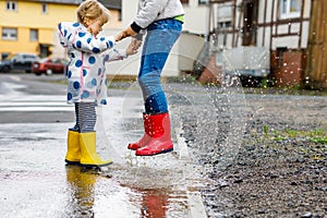 Close-up of two children, toddler girl and kid boy wearing red and yellow rain boots, walking during sleet. Happy