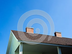 Close up two chimneys bricks on the roof of the light green wooden house against blue sky background.