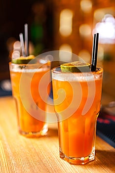 Close-up of two colorful orange cocktails with lime and brown sugar in bar.