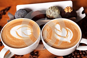 Two cappuccino cups with latte-art on a wooden table with scattered coffee beans and cakes. Joy with a Cup of coffee