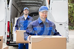 Close-up Of Two Delivery Men Carrying Cardboard Box