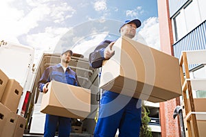 Close-up Of Two Delivery Men Carrying Cardboard Box photo