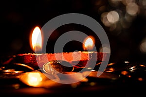 Close-up of two earthen lamps with flames, and shining coins below. Diwali and Dhan-teras concept
