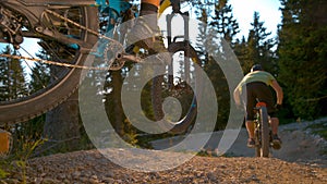 CLOSE UP: Two extreme mountain bike riders speed along an empty gravel track.