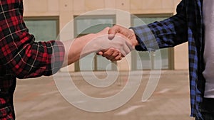 Close-up of two friends shaking hands in the city near modern building.