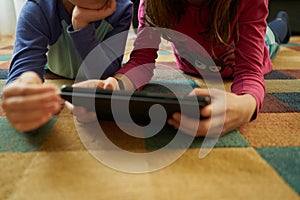 Close-up of two girls playing on the living room carpet with a tablet