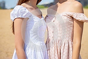 Close up of two girls in summer dresses stand together against the background of beach on sunny summer day