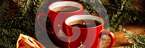 Close-up two glass cups full of hot, red, aromatic lemon tea with dark chocolate on a pine branch and table background. Winter sna