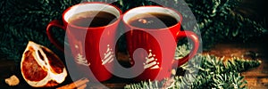 Close-up two glass cups full of hot, red, aromatic lemon tea with dark chocolate on a pine branch and table background. Winter sna