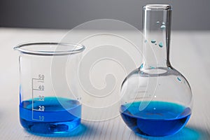 Close-up of two glass test tubes with blue liquid, on white wooden table and gray background, horizontally