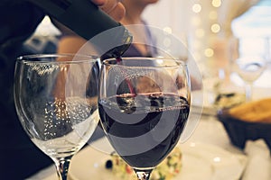 Close up of two glasses on a restaurant table with glasses at a formal dinner party. Filling wineglass with red wine at a festive