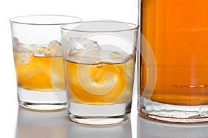 Close up on two glasses of whiskey on the rocks, with a whiskey bottle in white background