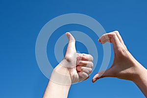 Close-up of two hands making a thumb up sign, half heart on a blue background, copy space. Friendzone concept, flirting