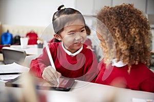 Close up of two kindergarten schoolgirls wearing school uniforms, sitting at a desk in a classroom using a tablet computer and sty photo