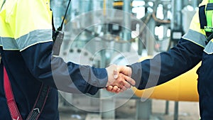 Close-up of two male labourer wearing uniform making handshake at heavy industry factory