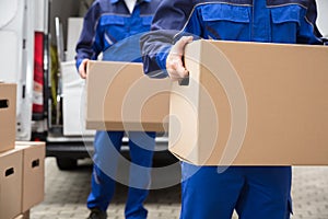 Close-up Of Two Movers Carrying Cardboard Box