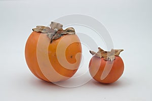 Close-up of two persimmon of different sizes on a white background