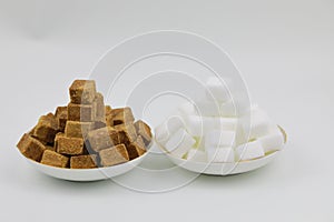 Close up two pile of brown sugar cubes on a white plate on white background