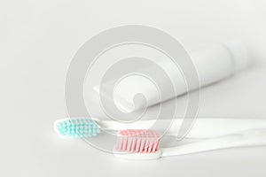 Close up of two plastic white toothbrushes with pink and blue bristle and toothpaste in tube.