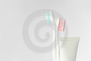 Close up of two plastic white toothbrushes with pink and blue bristle and toothpaste in tube on white background.