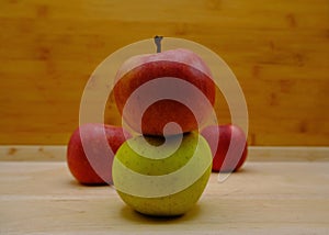 Close-up of two red and green apples, on top of a wooden surface, with other fruit in the background
