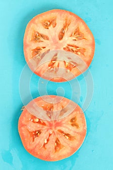 Close up of two round red tomato slices on blue background, fresh summer mood.